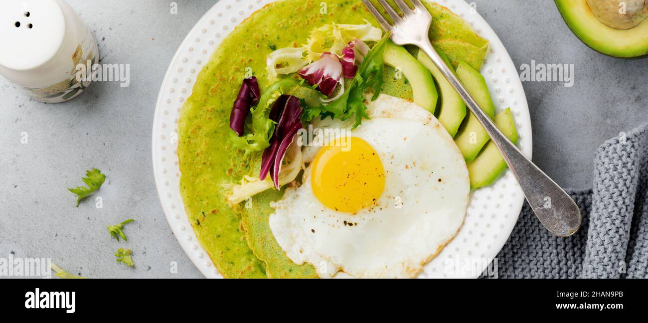 Crêpes vertes aux épinards (crêpes) avec œuf frit, avocat et feuilles de mélange de salade sur plaque de céramique sur fond de béton gris.Concept de sain br Banque D'Images