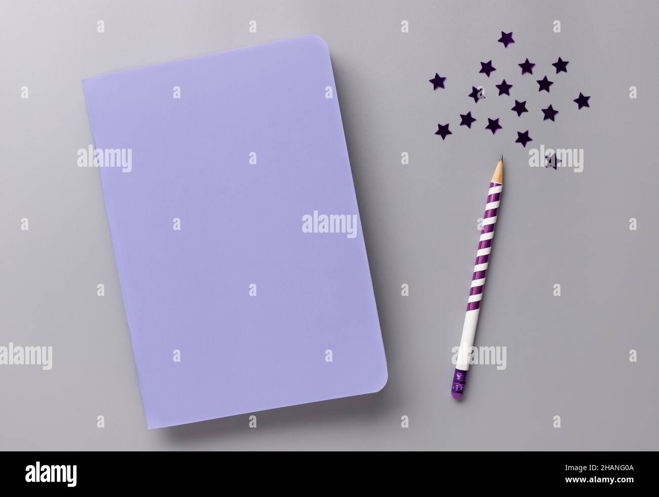 carnet blanc violet, crayon et confettis étoiles sur bureau gris Banque D'Images