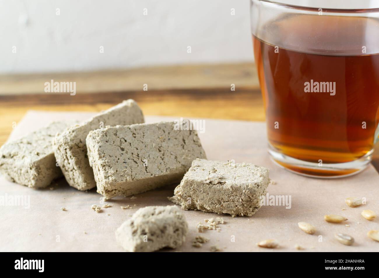 Plusieurs morceaux de tournesol halvah sur un papier à pâtisserie avec une tasse de thé sur une table en bois dans la cuisine.Style rustique.Bonbons naturels traditionnels. Banque D'Images