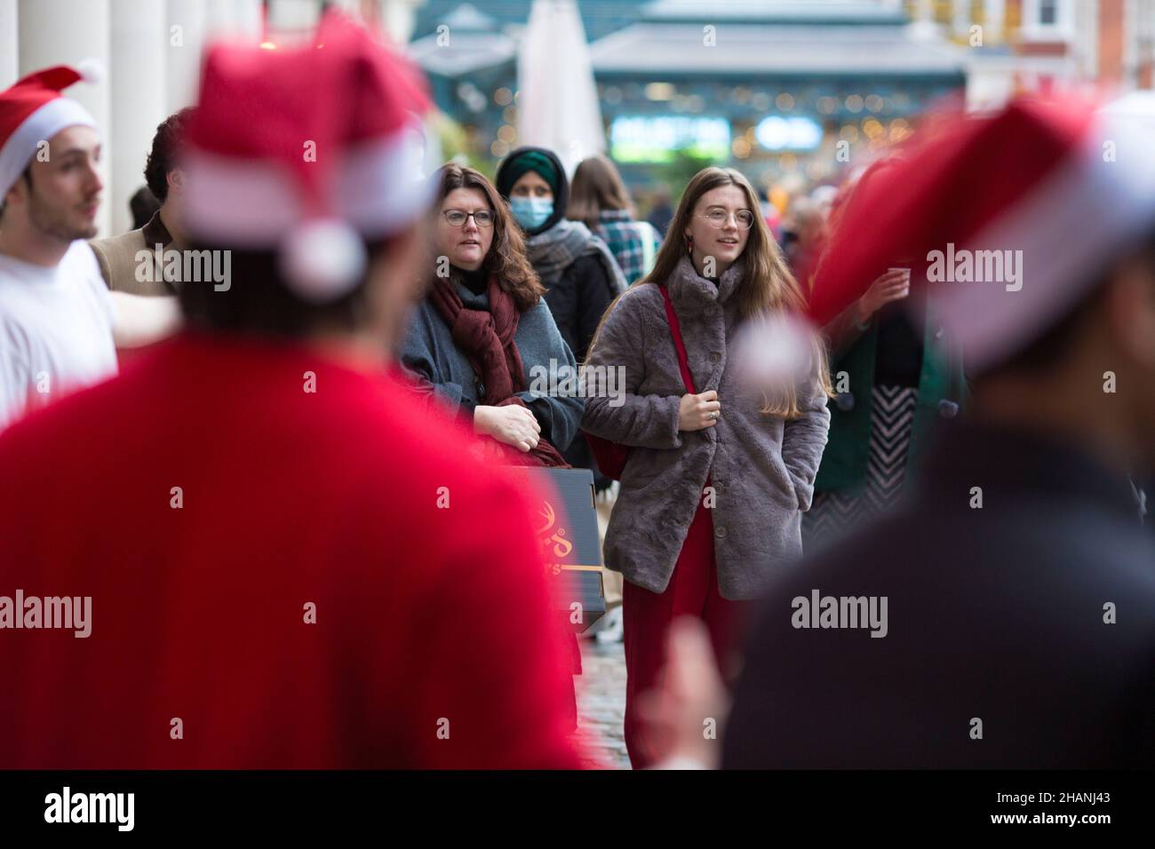 Les clients regardent des artistes portant des chapeaux de Père Noël dans le Covent Garden, dans le centre de Londres. Banque D'Images