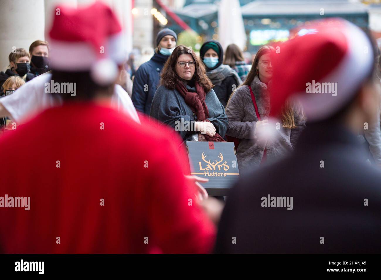 Les clients regardent des artistes portant des chapeaux de Père Noël dans le Covent Garden, dans le centre de Londres. Banque D'Images