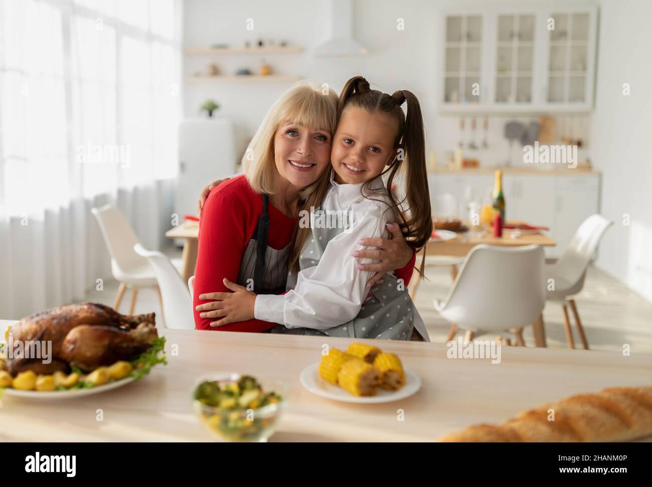 Portrait de la petite fille gaie et de sa grand-mère en tabliers cuisant le dîner de Noël, posant et embrassant dans la cuisine Banque D'Images