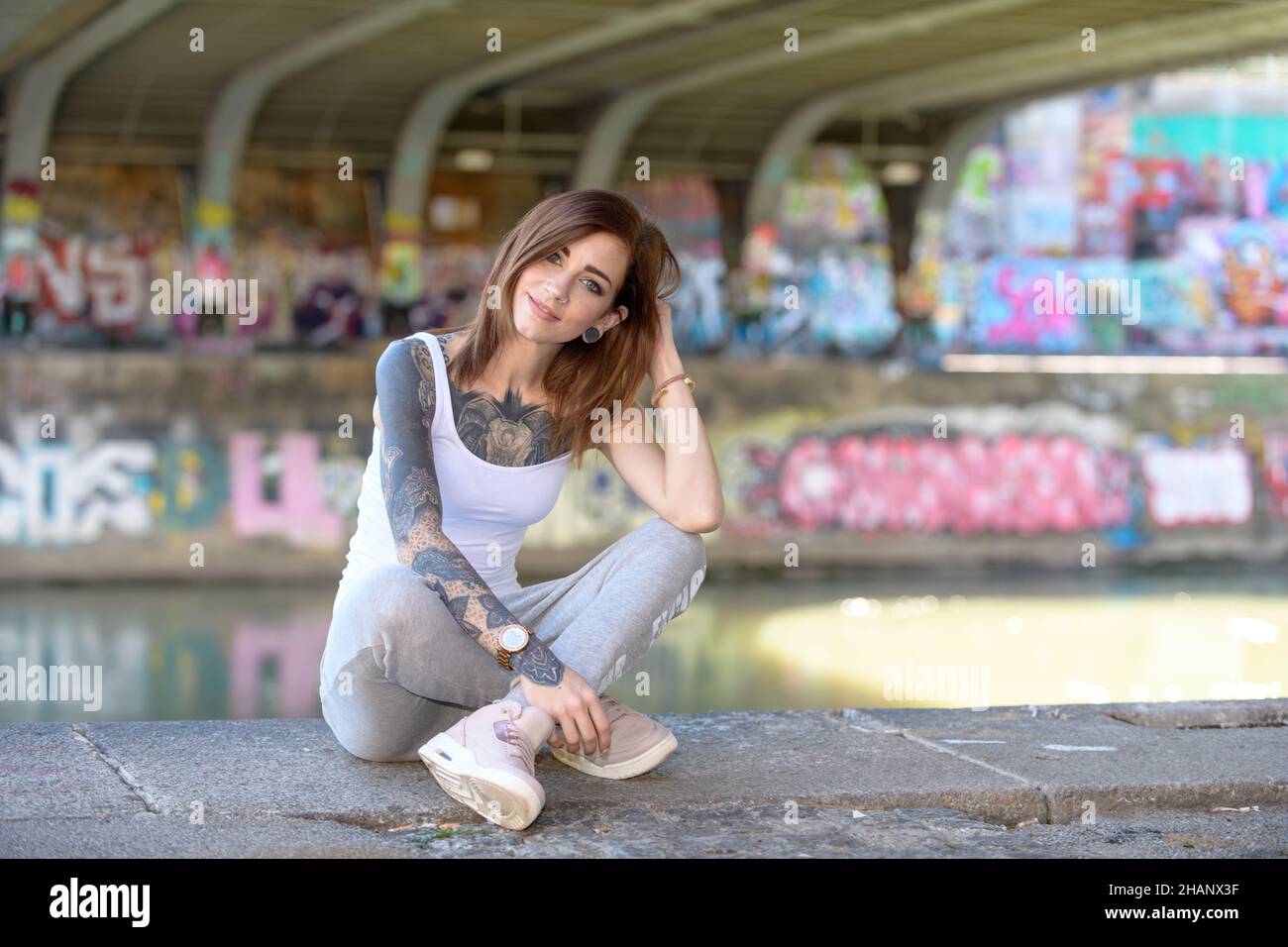 Une belle jeune femme tatouée est assise sur le sol à côté d'une rivière et profite de l'été chaud. Banque D'Images
