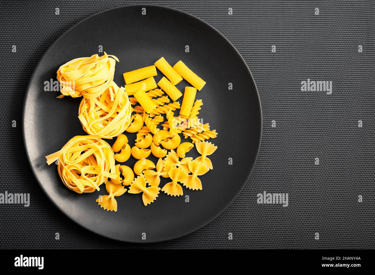 divers types de pâtes comme la fettuccine, le fusilli, le farfalle sur une assiette noire Banque D'Images