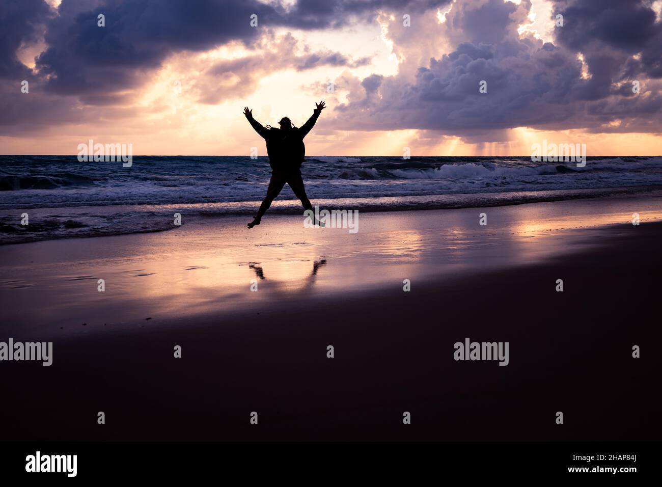 Silhouette d'un jeune homme qui saute au bord de la mer avec les bras et les jambes étirés pendant le lever du soleil. Banque D'Images