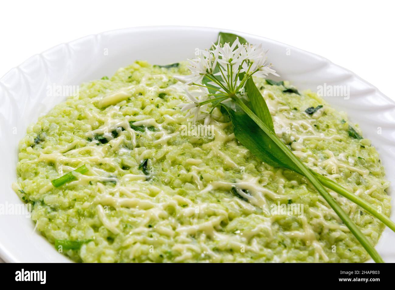 Risotto Ramsons (poireau d'ail sauvage) au parmesan, servi dans une assiette blanche avec des feuilles de ramson fraîches et des fleurs comme décoration sur le backgrou blanc Banque D'Images