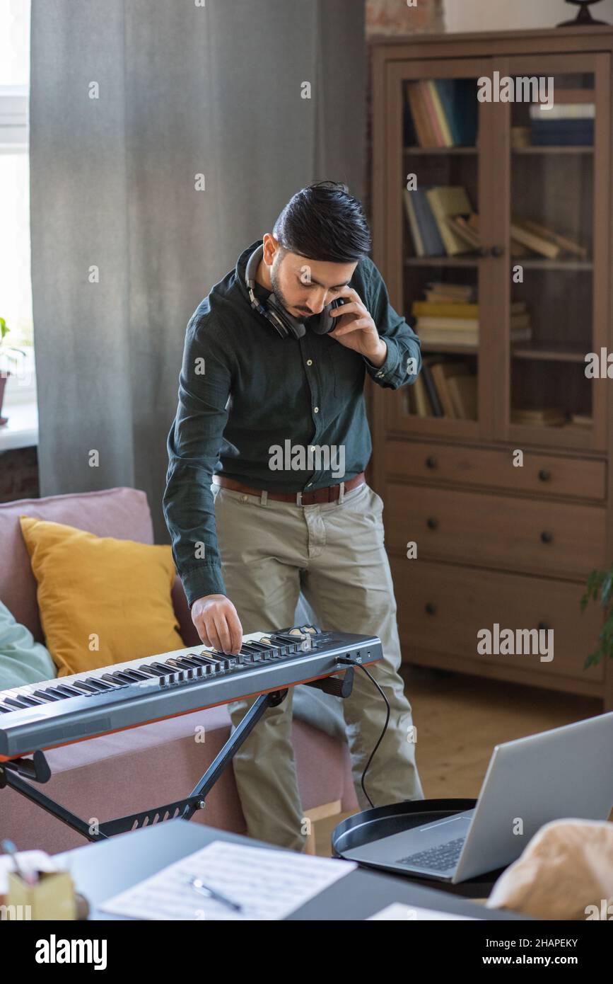 Jeune homme parlant sur téléphone portable tout en se tenant près du  clavier de piano devant l'ordinateur portable dans le milieu de la maison  Photo Stock - Alamy