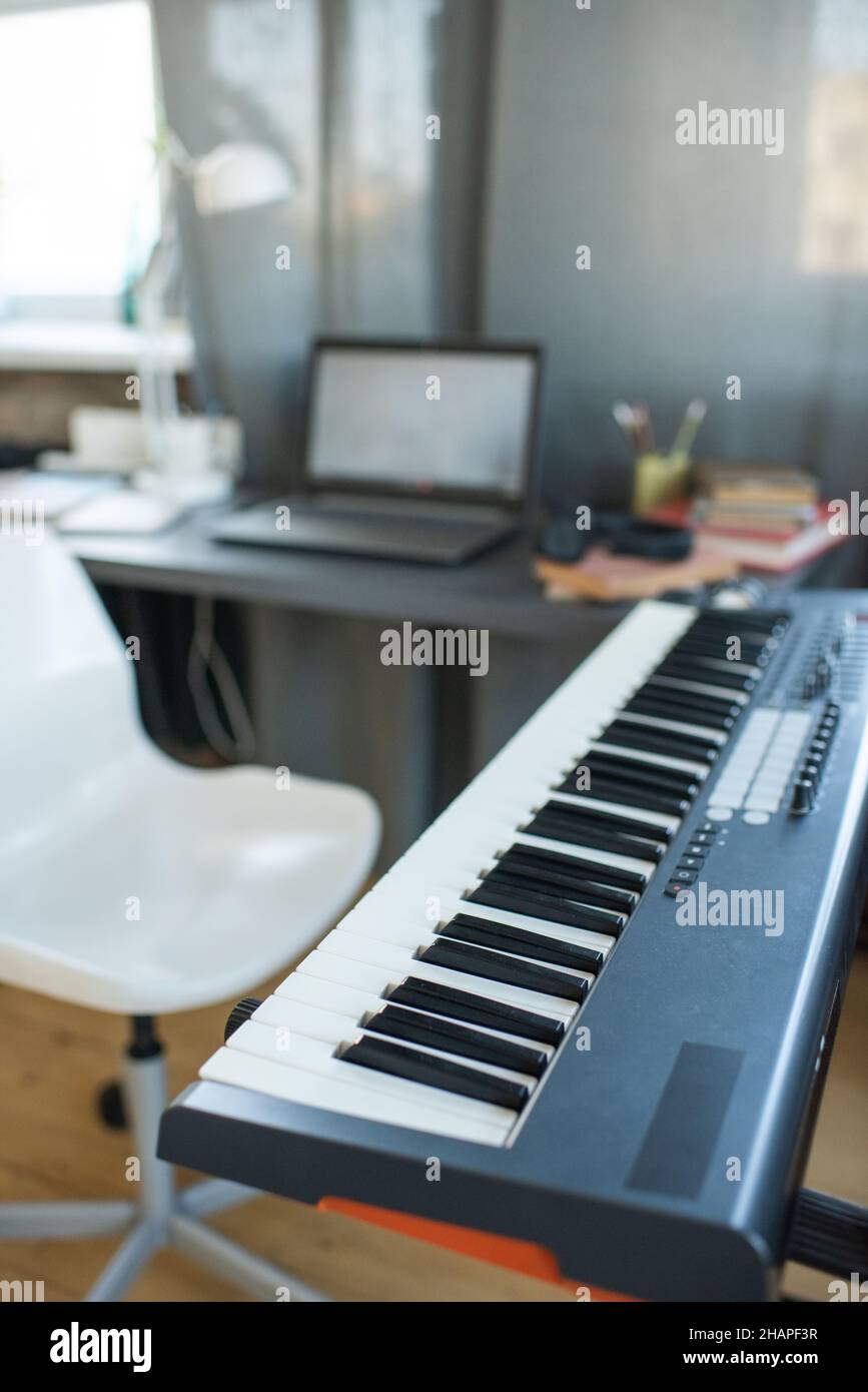 Lieu de travail de musicien ou étudiant contemporain avec clavier de piano, fauteuil et bureau avec ordinateur portable dans un environnement familial Banque D'Images