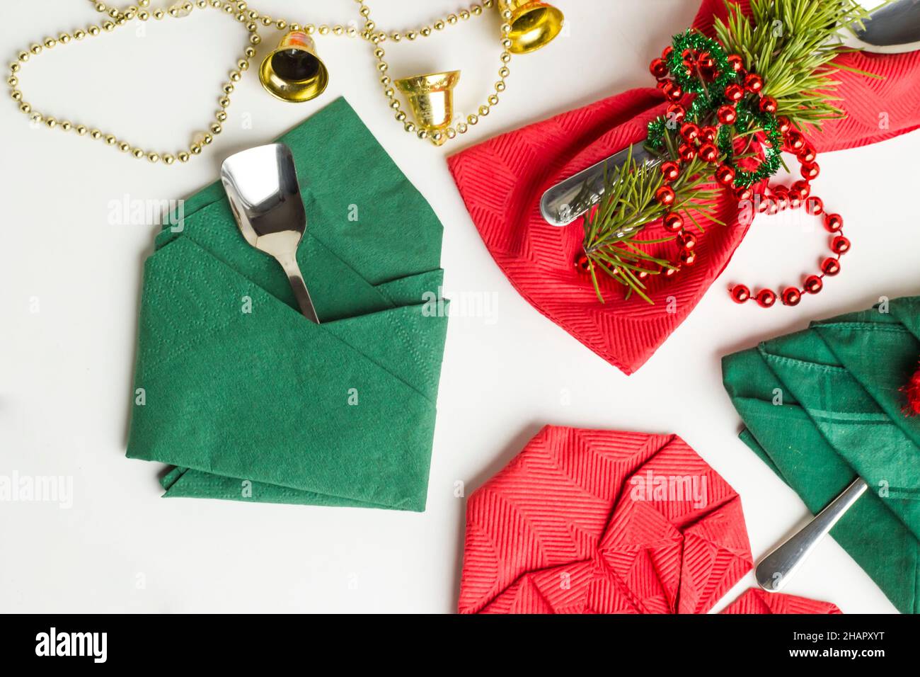 Serviettes de Noël rouges et vertes pliées en différentes formes sur une surface blanche avec ensemble de couverts, ronds de serviettes et décorations de noël Banque D'Images
