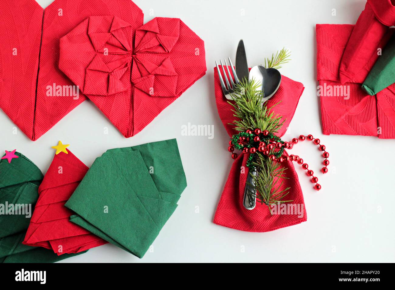 Serviettes de Noël rouges et vertes pliées en différentes formes sur une surface blanche avec ensemble de couverts, ronds de serviettes et décorations de noël Banque D'Images