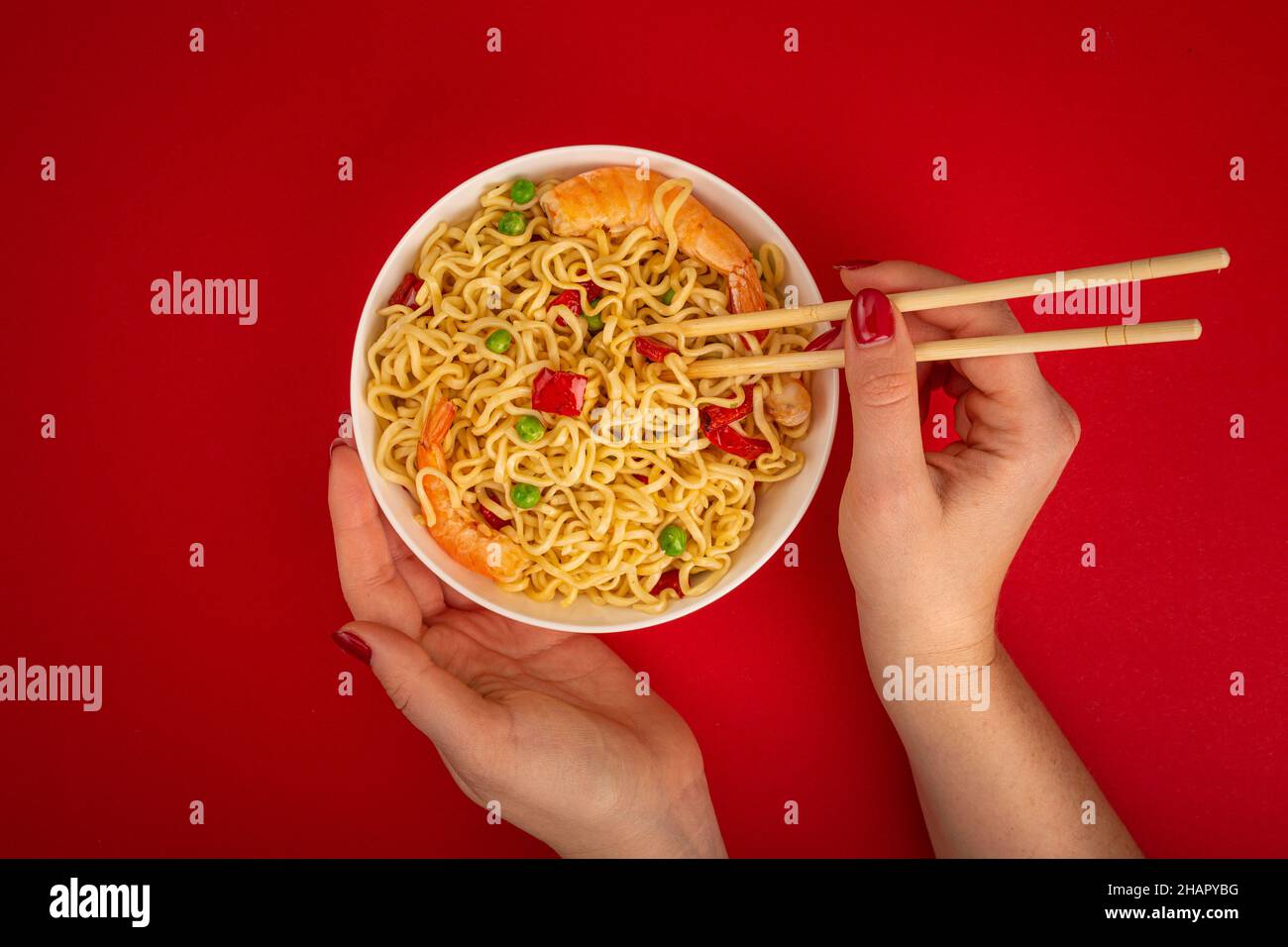 Mains de femmes avec un bol de nouilles aux crevettes sur fond rouge Banque D'Images