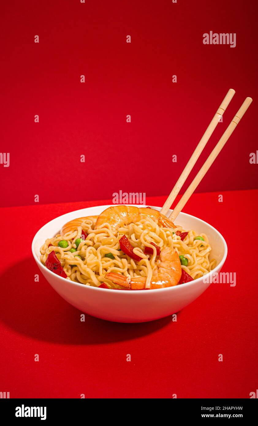 Nouilles asiatiques avec crevettes dans un bol, fond rouge minimal Banque D'Images
