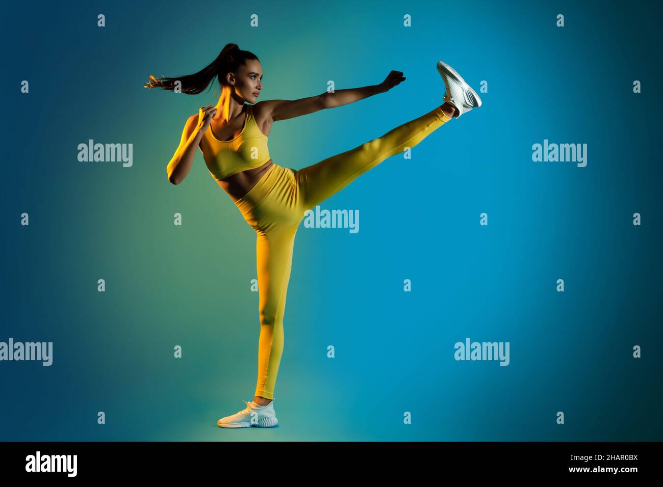 Femme faisant Karate coup de pied de côté levant la jambe clatching Fists, Studio Banque D'Images