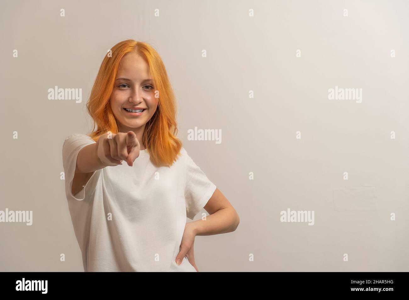 jeune fille avec des cheveux rouges dans un t-shirt blanc sur un fond clair pointe le doigt vers l'avant. Banque D'Images
