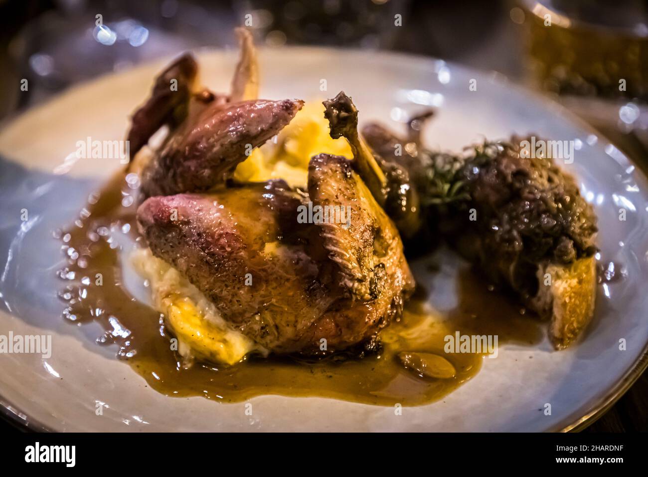 Un morceau de volaille croustillamment rôti, probablement une caille, reposant avec une purée de pommes de terre et un jus foncé sur une assiette blanche au Restaurant Hestia à Bormes-les-Mimosas, dans le Var, France. Banque D'Images