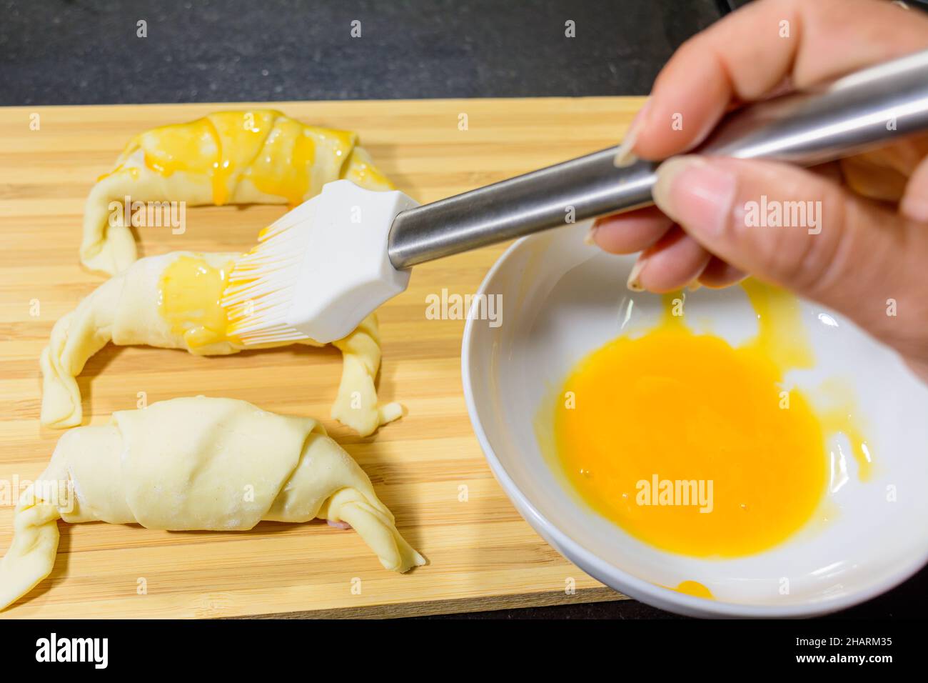 Chef peignant les croissants au jambon et au fromage avec du jaune d'œuf sur une planche en bois Banque D'Images