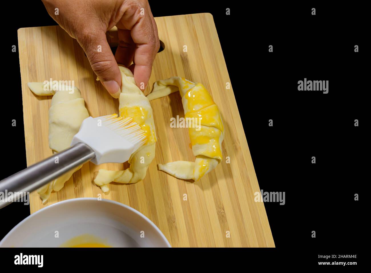 Chef peignant les croissants avec du jaune d'œuf sur une planche en bois Banque D'Images