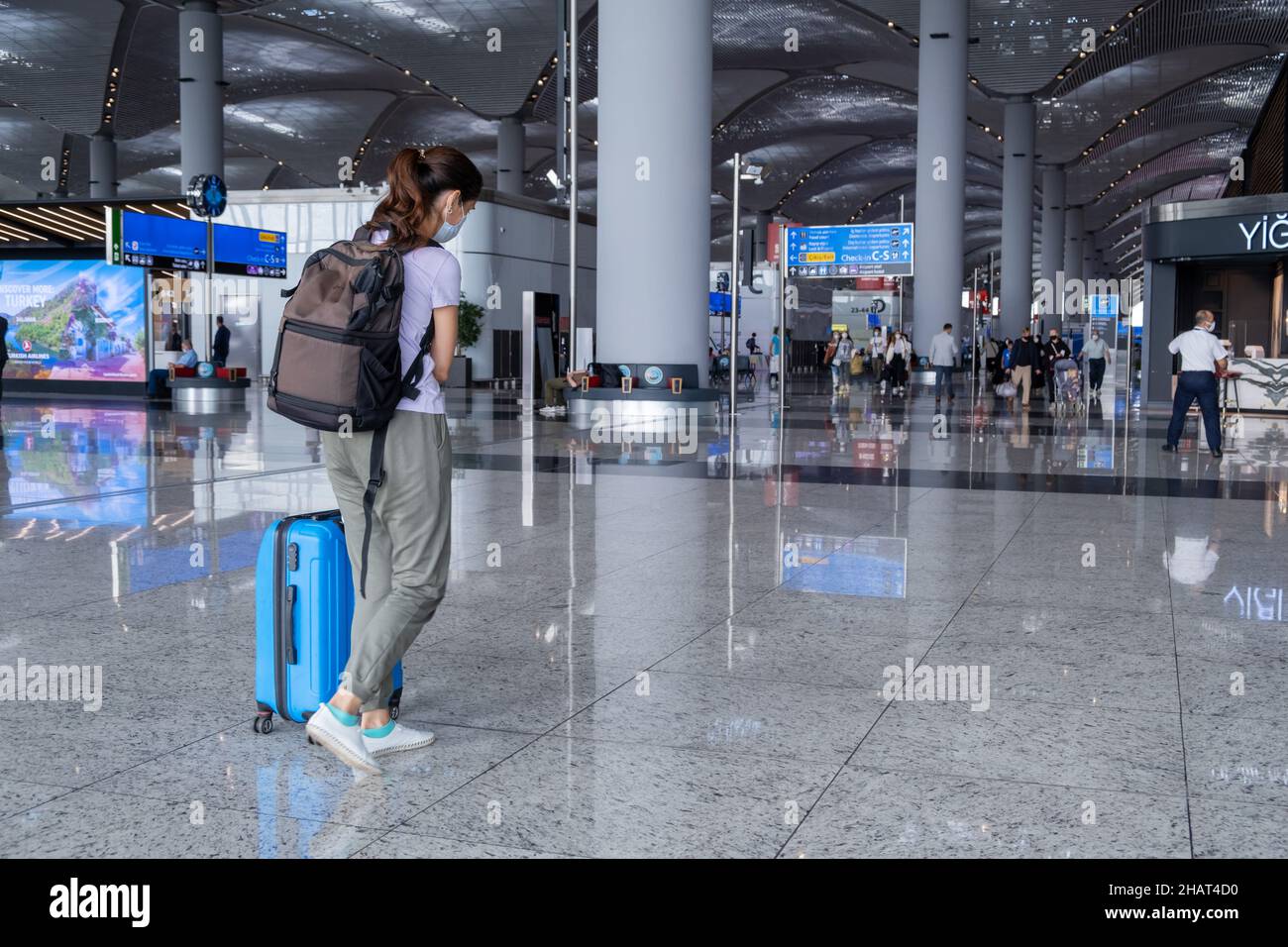 ISTANBUL, TURQUIE - 7 septembre 2021 : une femme tire une valise bleue dans le terminal de l'aéroport d'Istanbul.Fille itinérante portant des vêtements décontractés et un masque avec Banque D'Images