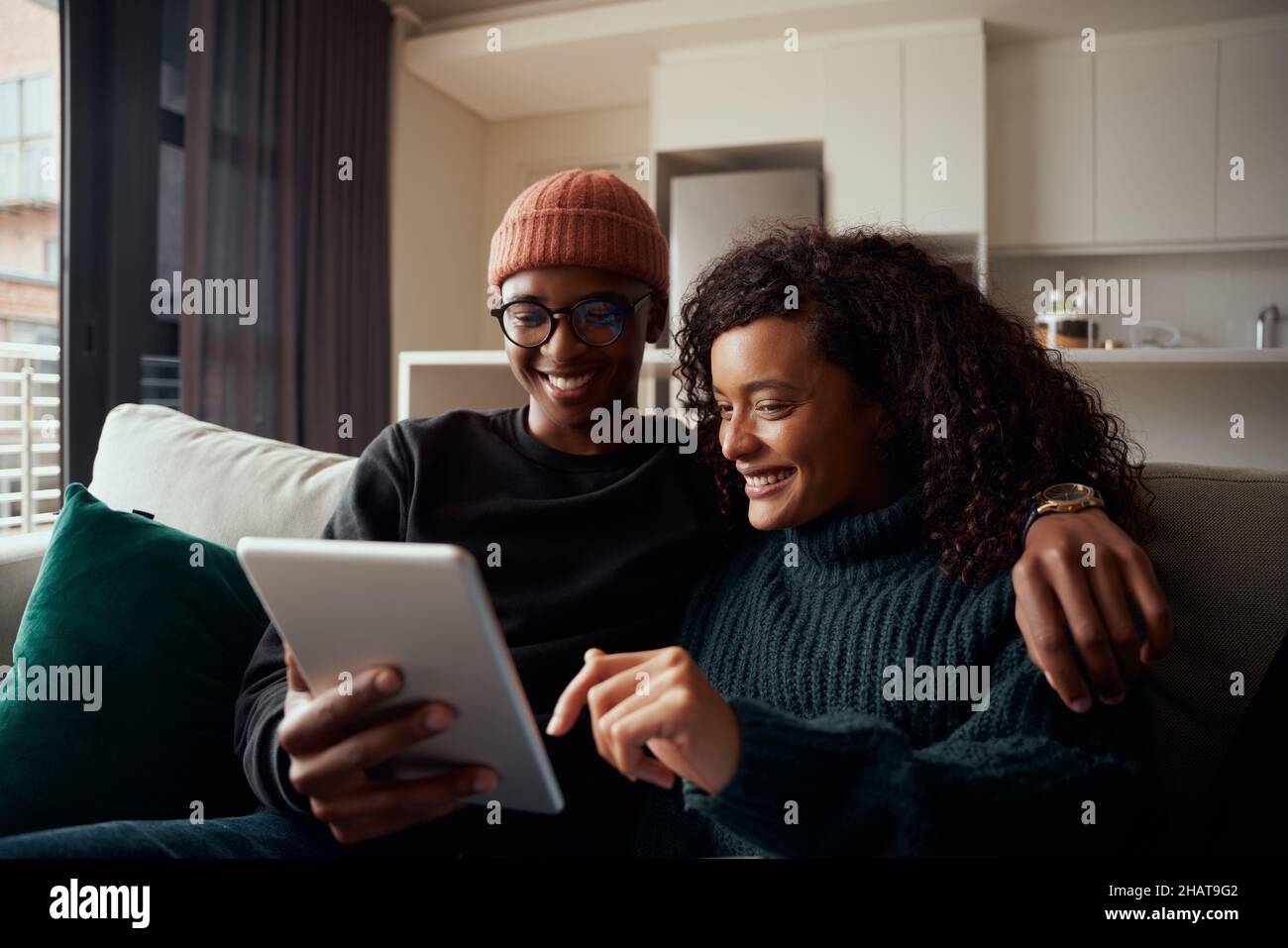 Couple adulte, multi-ethnique, souriant tout en utilisant le tabe sur le canapé dans l'appartement moderne Banque D'Images