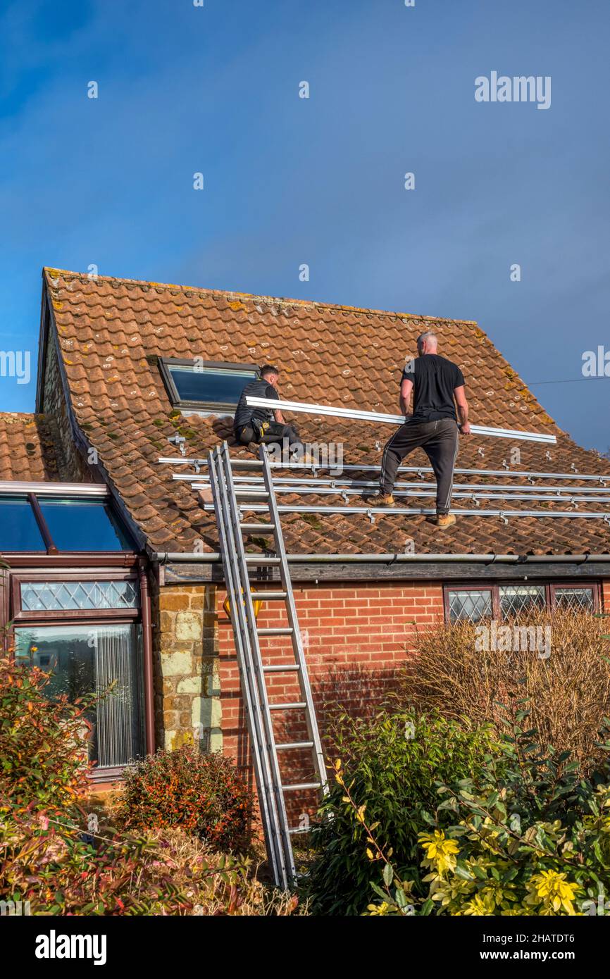 Les travailleurs qui installent des panneaux solaires ou des cellules photovoltaïques sur le toit en tuiles pantiées d'un chalet de Norfolk.NB: Les locaux dans la photographie sont la propriété libérée. Banque D'Images