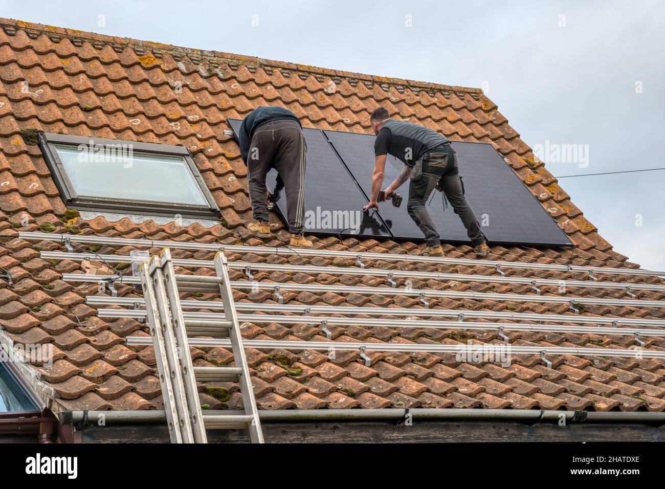 Les travailleurs qui installent des panneaux solaires ou des cellules photovoltaïques sur le toit en tuiles pantiées d'un chalet de Norfolk.NB: Les locaux dans la photographie sont la propriété libérée. Banque D'Images