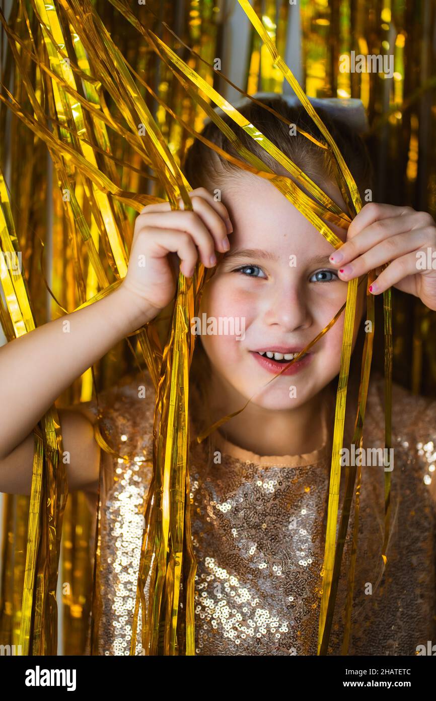 Jolie petite fille blonde portant une robe chic souriante sur fond doré scintillant. Banque D'Images