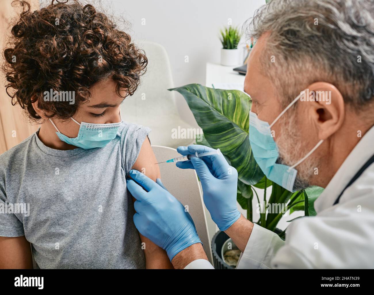 Vaccinations de routine pour un enfant.Un garçon aux cheveux bouclés portant un masque médical lorsqu'il est vacciné par un pédiatre mature à la clinique médicale Banque D'Images