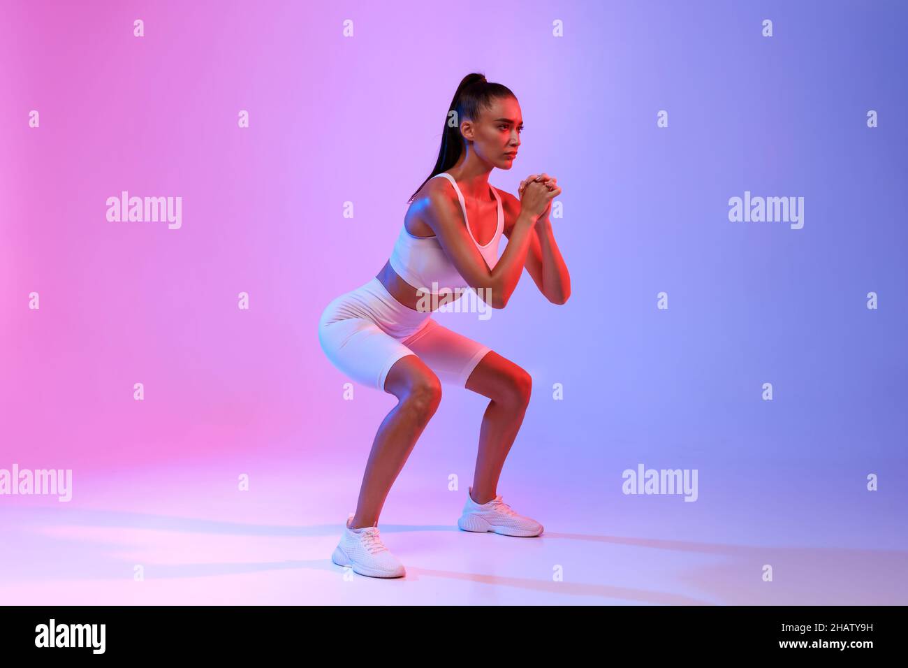 Femme faisant de l'exercice profond de Squat sur Neon Studio Background Banque D'Images