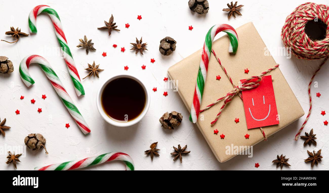 Une tasse de thé, une boîte cadeau avec une étiquette rouge, quelques cannes de Noël, de petites étoiles rouges, de l'anis étoilé, des cônes de pin et une boule de fil rouge et beige. Banque D'Images
