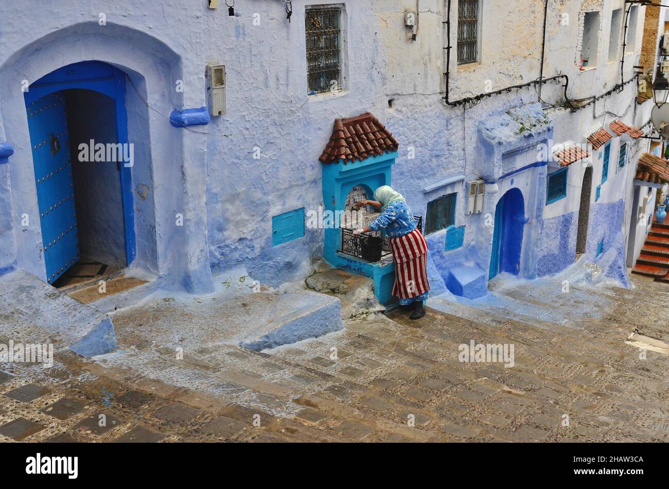 Femme bien dans une allée avec des escaliers, vieille femme tirant bien l'eau devant la maison, Chefchaouen, Tanger-Tétouan-Al Hoceima, Maroc Banque D'Images