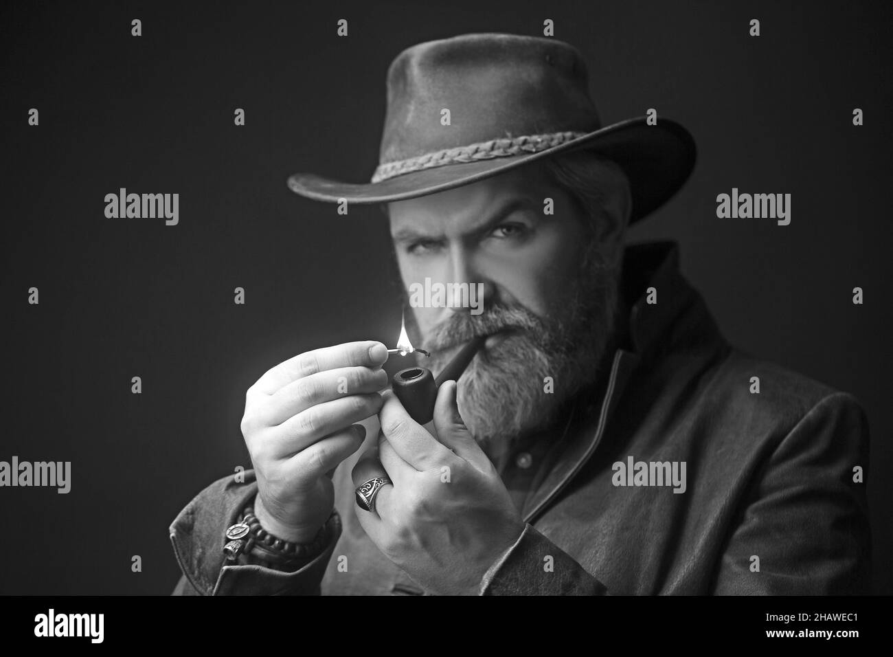 Pipe fumant vintage caractéristique cow-boy homme avec les cheveux gris et la barbe. Studio tourné sur fond sombre. Banque D'Images