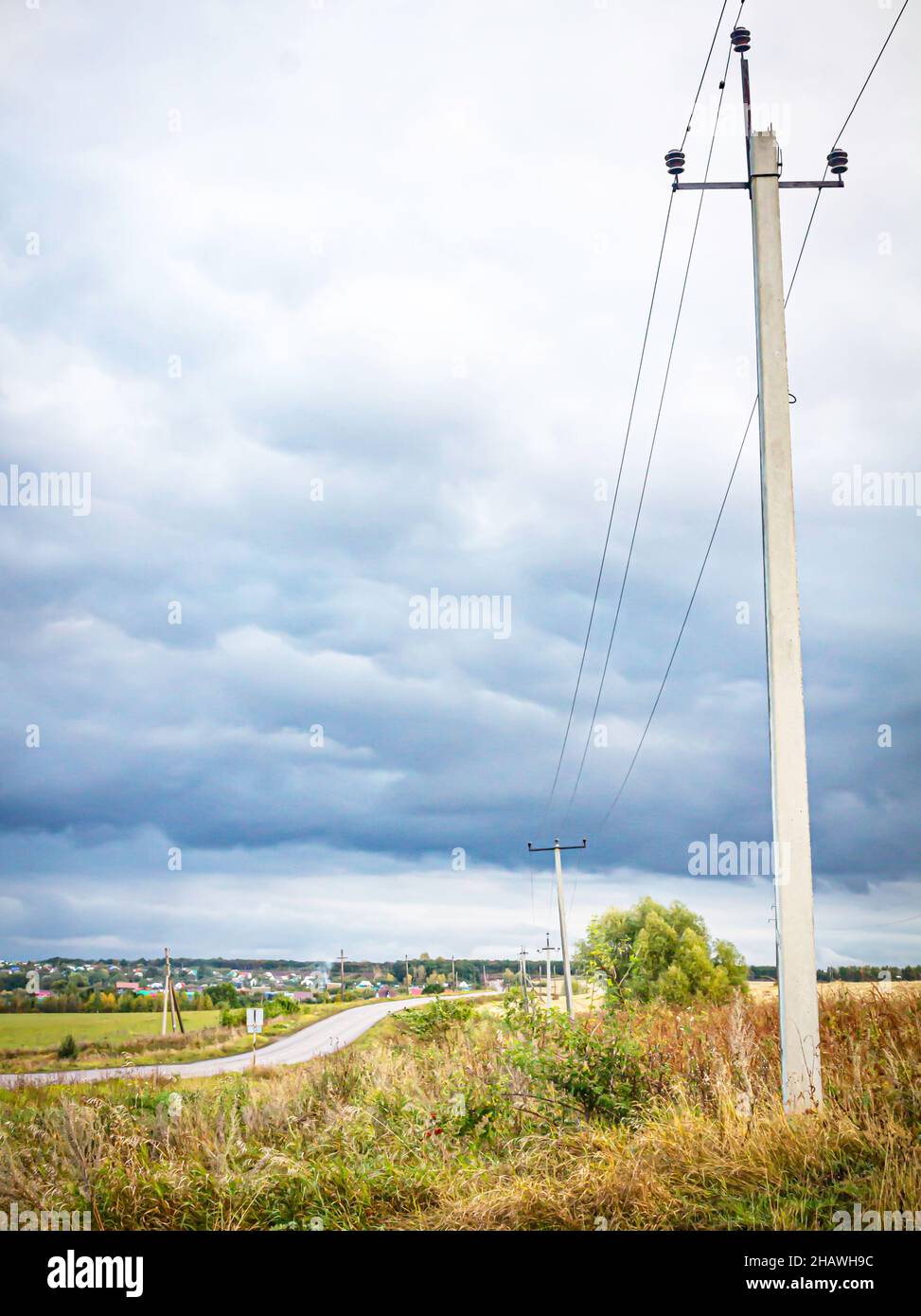 Route d'asphalte rurale dans les champs menant à des chalets de campagne d'été sous des nuages sombres de tempête Banque D'Images