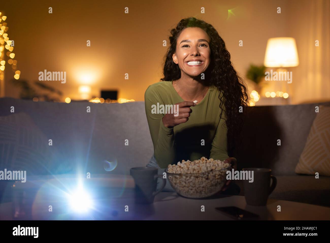 Femme regardant un film sur un projecteur et en train de manger du maïs soufflé à la maison Banque D'Images