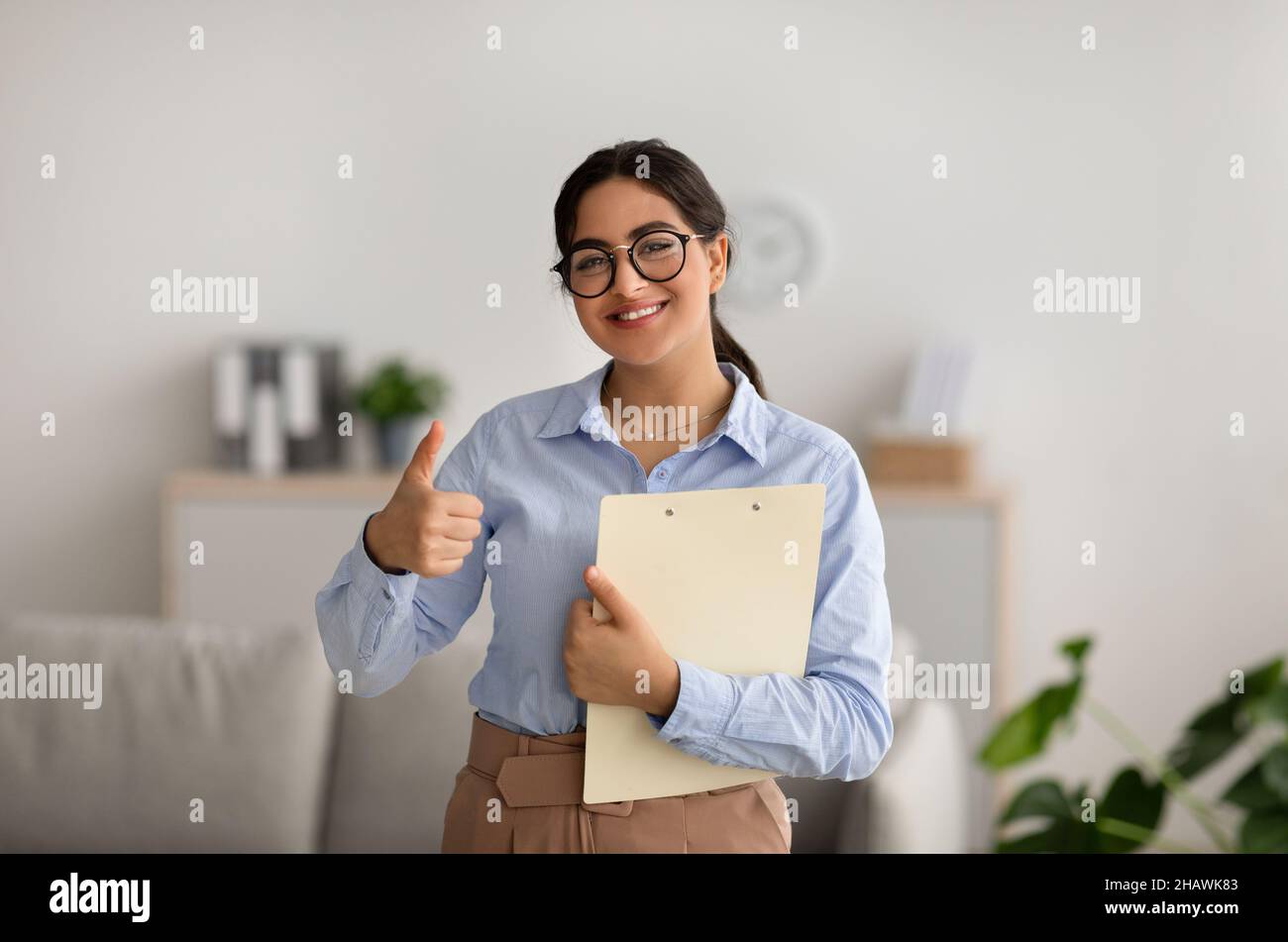 Une psychologue féminine positive se fait le geste du pouce, travaille au bureau et sourit, recommandant un cours de formation Banque D'Images