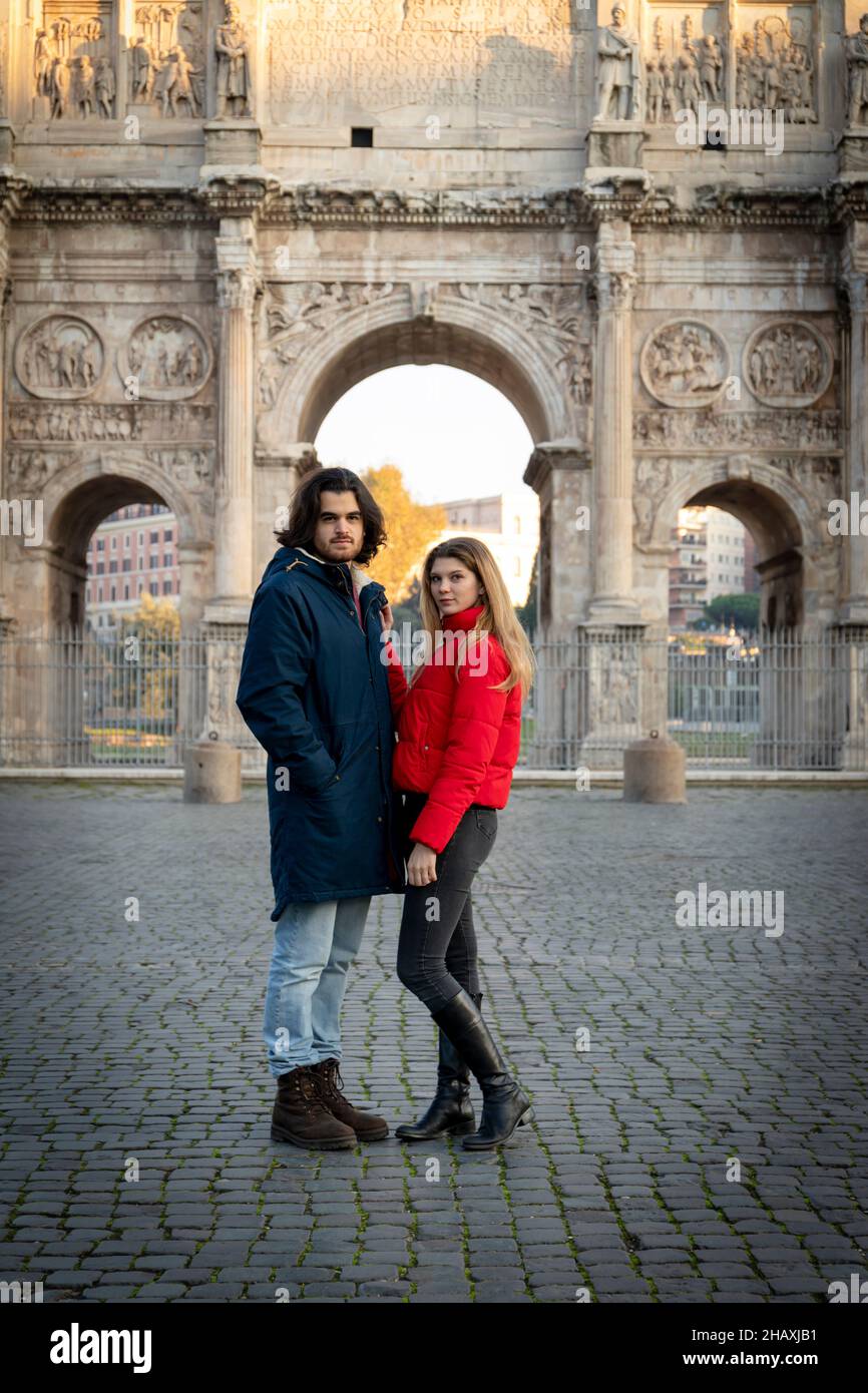 Jeune couple en voyage à Rome.Le jeune couple pose devant l'Arche de Titus.La blonde dans sa veste rouge met sa main sur son boyfrien Banque D'Images