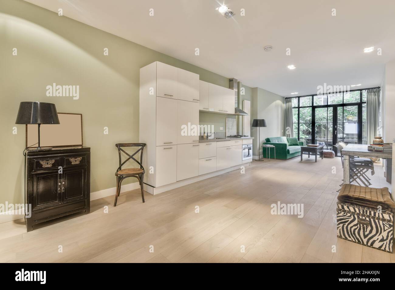 Intérieur d'une cuisine contemporaine spacieuse avec parquet beige laminé, mobilier blanc, hotte en acier inoxydable et four à gaz intégré avec cuisinière Banque D'Images