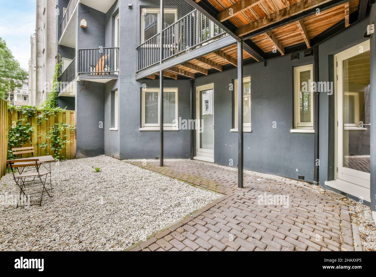 Extérieur de maison résidentielle moderne avec patio arrière-cour avec zone de loisirs avec table et chaises en bois et plantes vertes poussant sur la clôture Banque D'Images