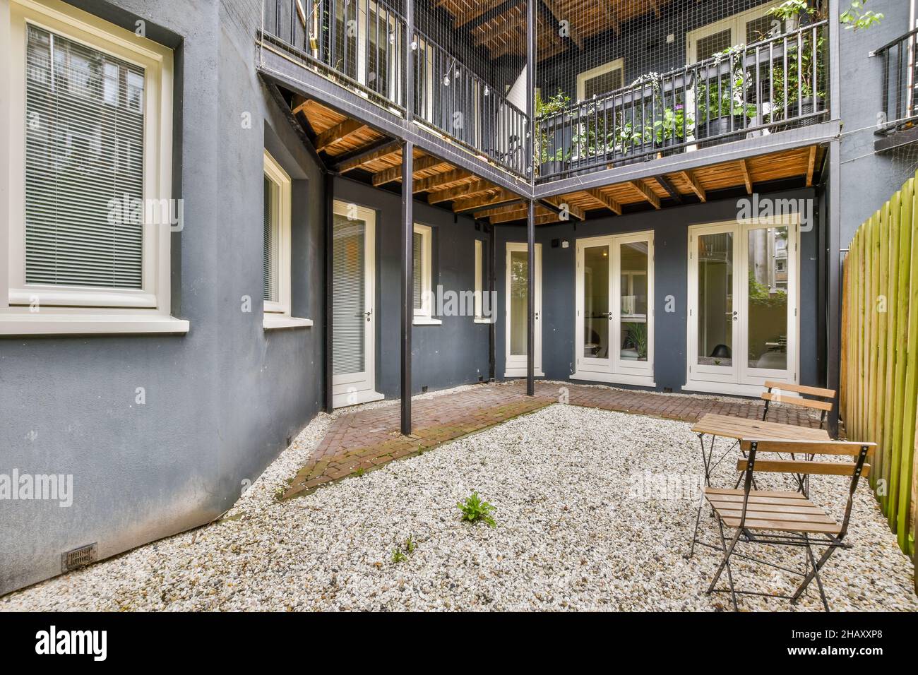 Extérieur de maison résidentielle moderne avec patio arrière-cour avec zone de loisirs avec table et chaises en bois et plantes vertes poussant sur la clôture Banque D'Images