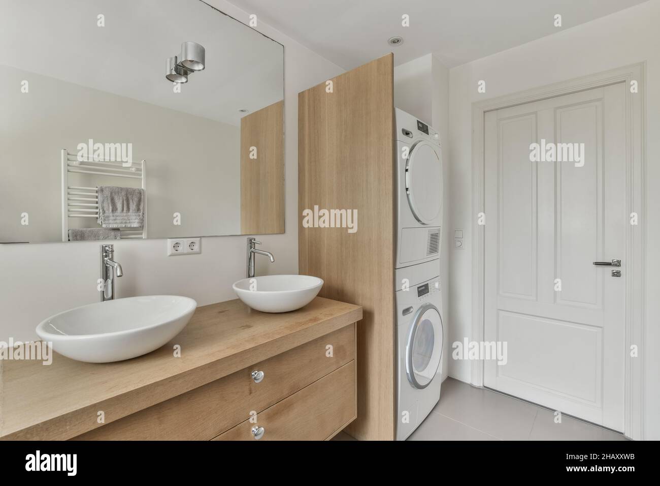 Armoire en bois avec double vasque lavabos au mur avec miroir dans la salle  de bains moderne lumineuse avec lave-linge contemporain près de porte  fermée Photo Stock - Alamy