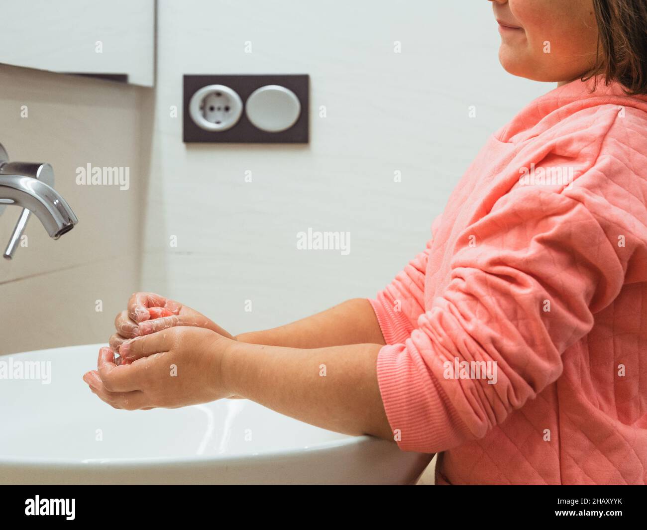 Vue latérale d'un enfant anonyme se lavant les mains à l'évier avec de l'eau du robinet pendant la routine d'hygiène quotidienne dans la salle de bains lumineuse à la maison Banque D'Images