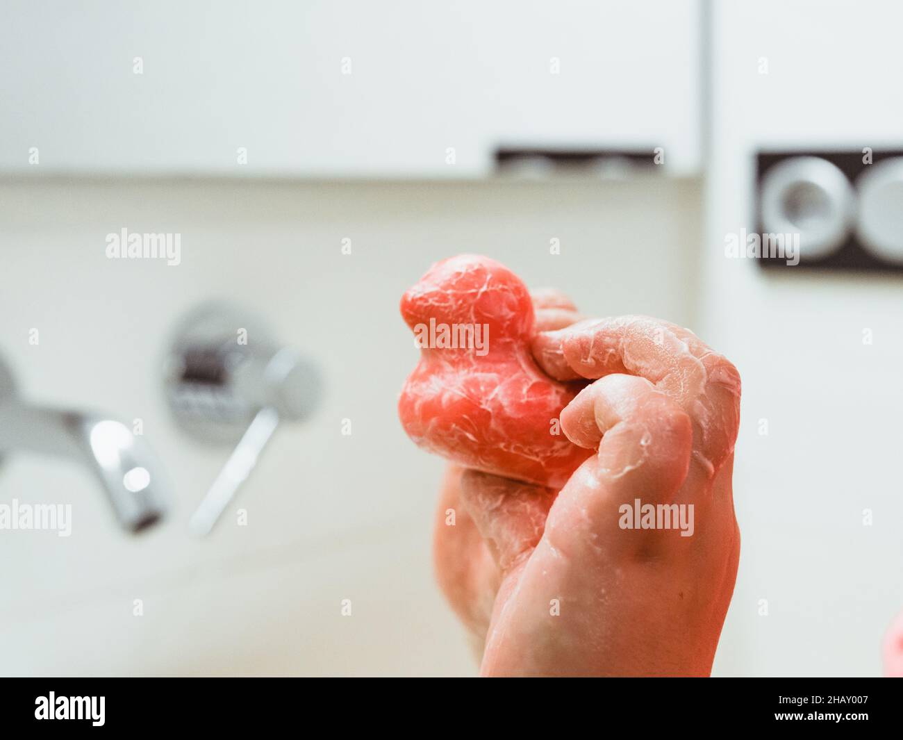 Crop enfant méconnaissable avec du savon en forme de canard rouge debout dans la salle de bains claire tout en se lavant les mains pendant la routine d'hygiène quotidienne à la maison Banque D'Images