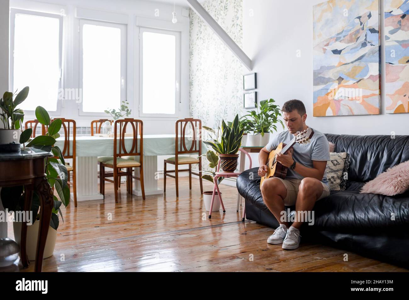 Corps complet de musicien masculin concentré jouant de la chanson sur  guitare acoustique tout en étant assis sur un canapé dans la chambre avec  une plante en pot Photo Stock - Alamy