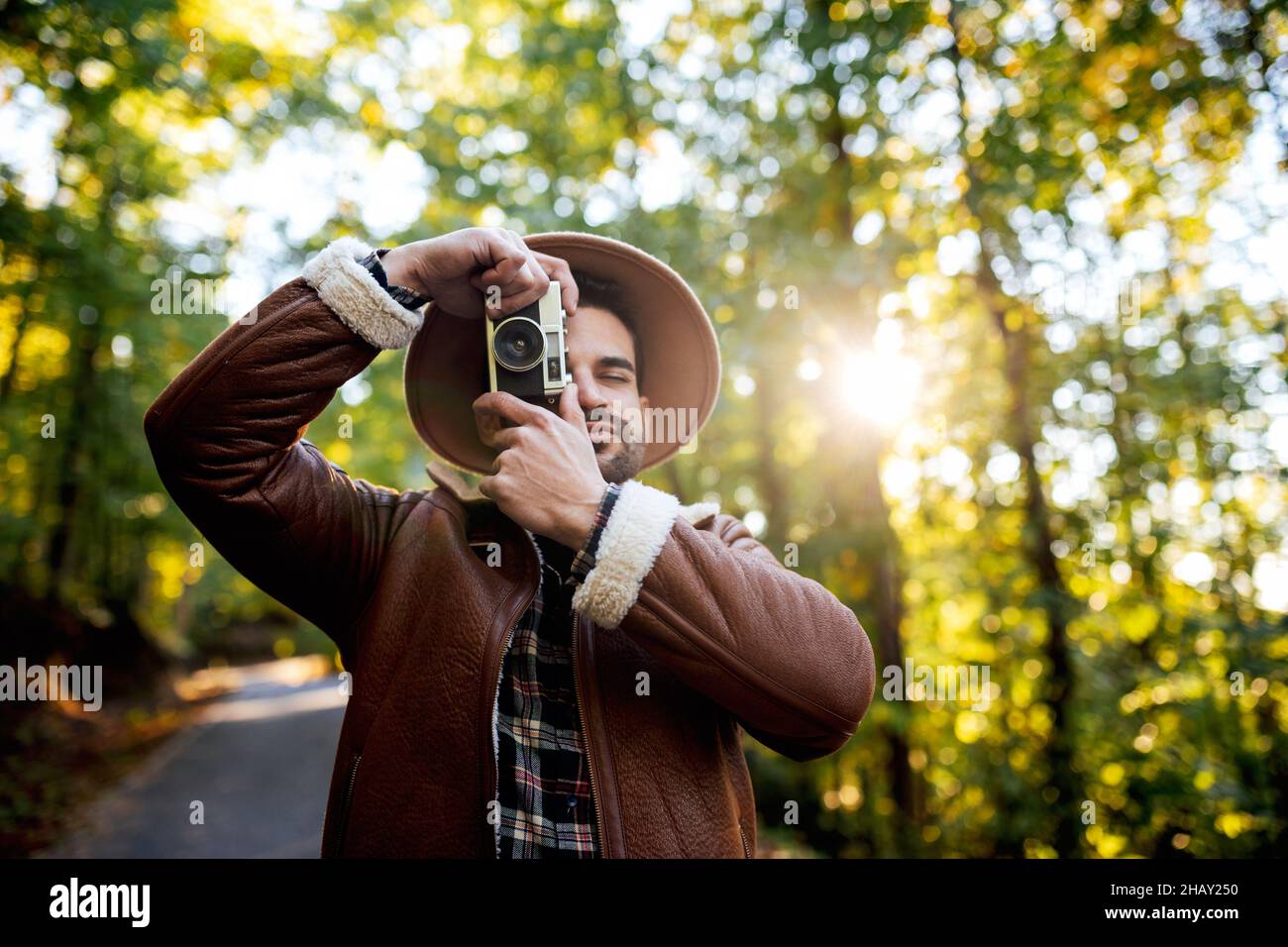 Photographe de style masculin prenant des photos avec un appareil photo d'époque de la nature tout en se tenant sur un chemin d'asphalte près de grands arbres verts pendant le voyage Banque D'Images