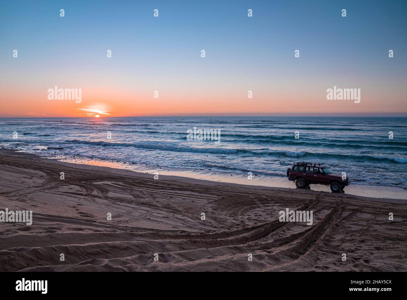 Voiture offroad rouge garée sur le rivage sur le sable à la plage pendant le coucher du soleil Banque D'Images