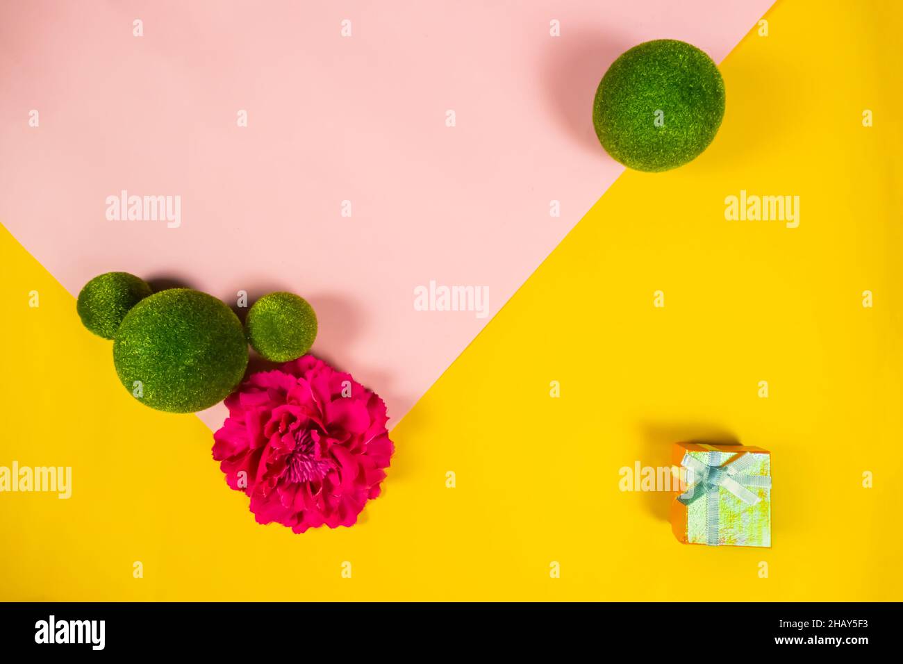 Contexte de la bannière de la Journée internationale de la femme. Boules vertes sur fond rose et jaune avec boîte cadeau et fleur. Cadre et fleurs. Manuscrite Banque D'Images