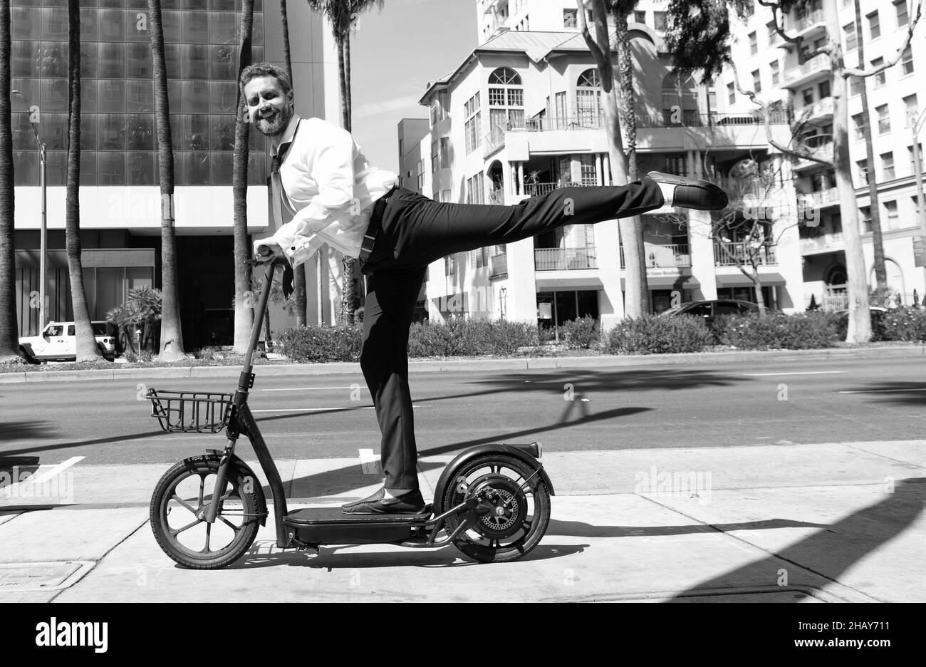 homme d'affaires heureux à cheval électro-scooter sur fond de paysage urbain, transport de location. Banque D'Images