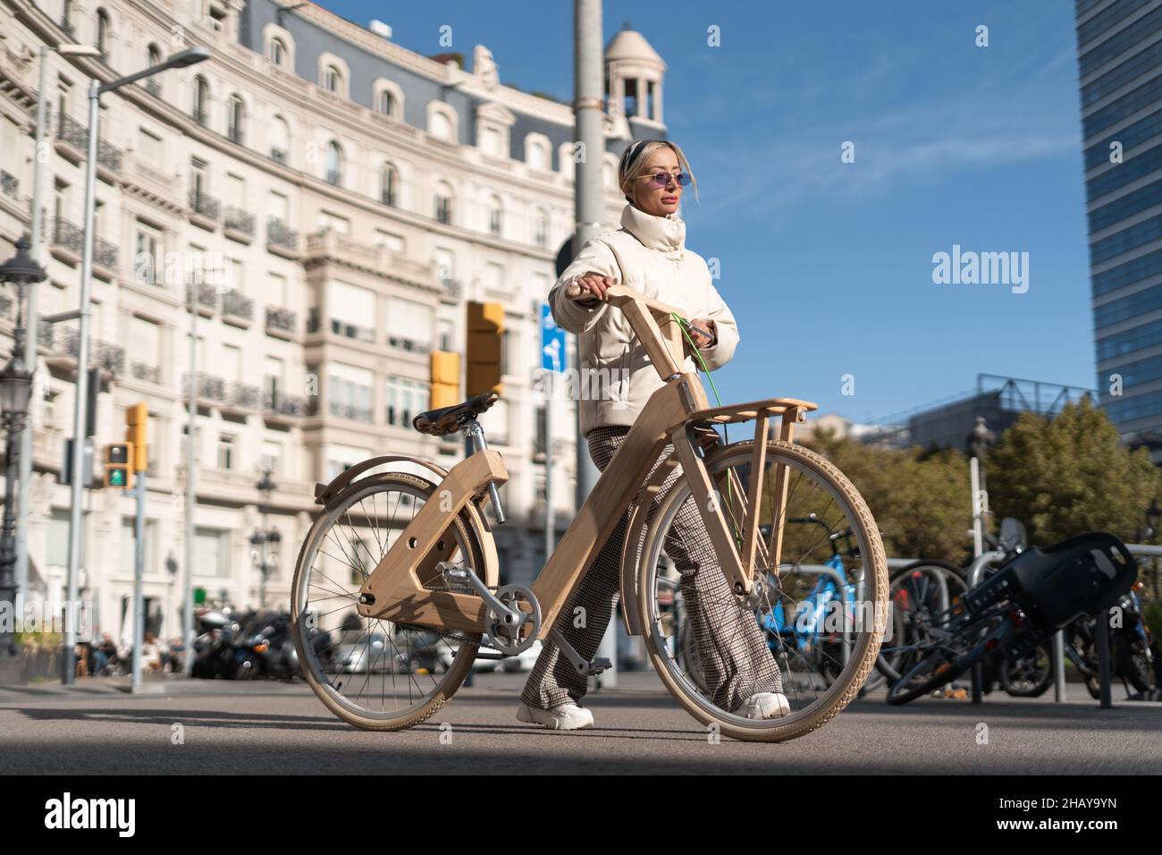 Femme adulte en vêtement d'extérieur à pied près de la bicyclette éco de bois le jour ensoleillé dans le centre-ville. Banque D'Images