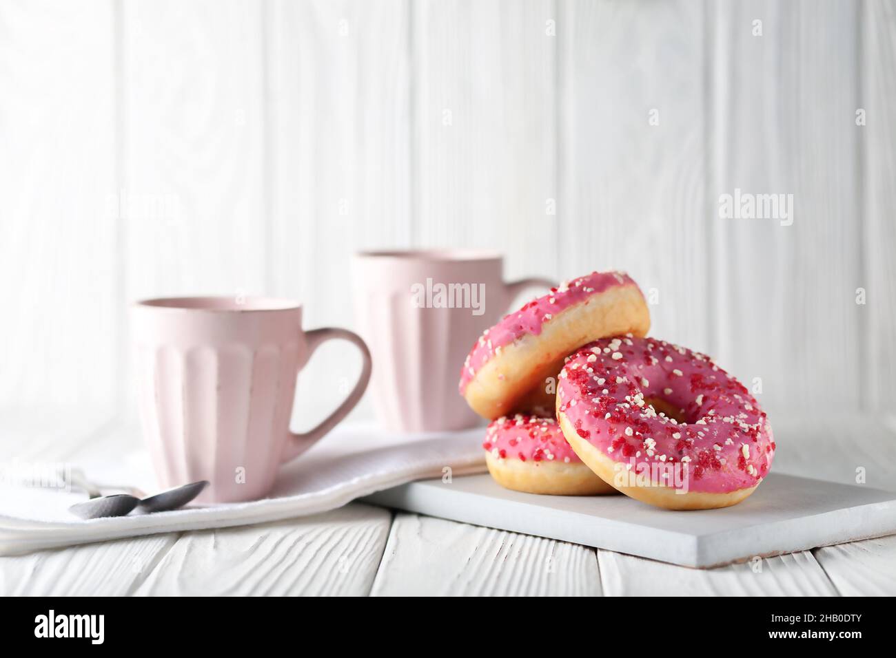 Beignets à la glaçure rose et à la poudre de caramel colorée sur fond blanc en bois. Banque D'Images