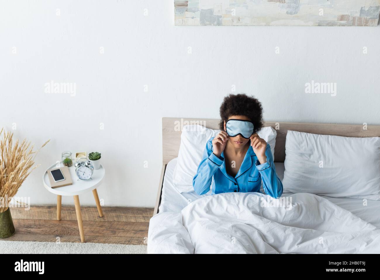 vue en grand angle de la femme afro-américaine qui règle le masque de sommeil dans la chambre Banque D'Images