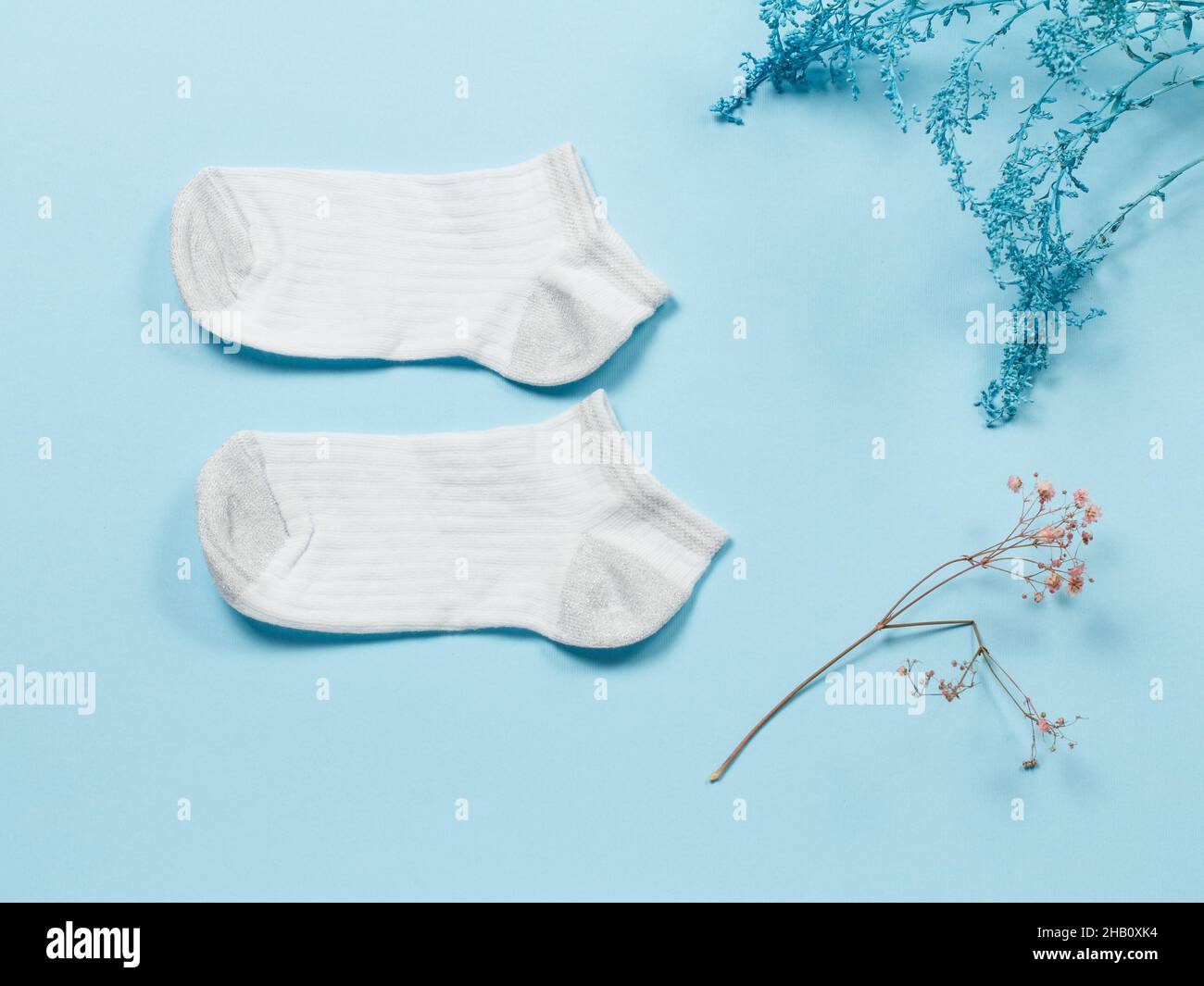 Paire de chaussettes blanches pour femmes et branches décoratives sur fond bleu, vue du dessus. Banque D'Images